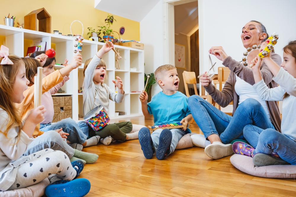 Kindergarten,teacher,with,children,sitting,on,the,floor,having,music