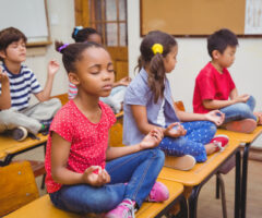 Pupils,meditating,in,lotus,position,on,desk,in,classroom,at